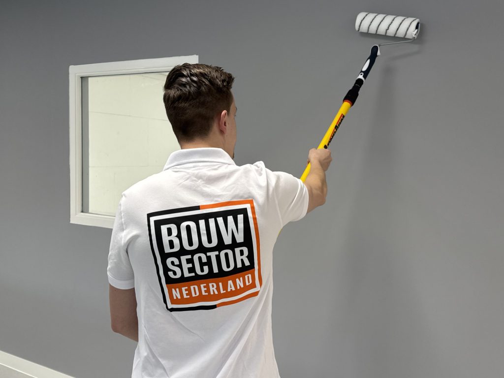 Schilder rolt een grijze muur strak tot aan een wit gelakt binnenkozijn