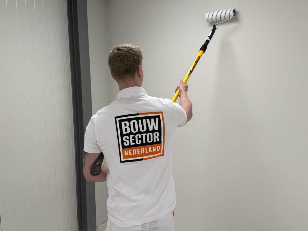 Schilder met het logo van Bouwsector Nederland op zijn polo rolt een wand in een lege ruimte
