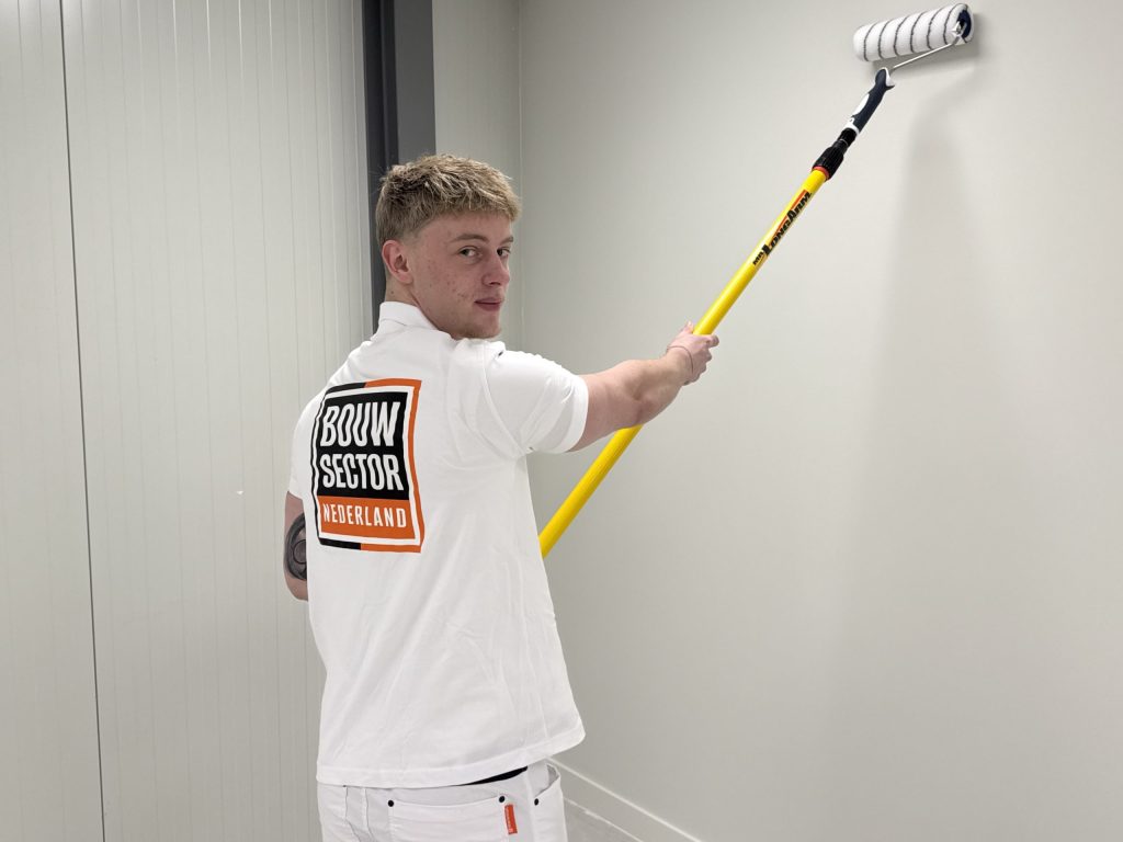 Schilder van Bouwsector Nederland kijkt om terwijl hij met de roller een lichte wand afwerkt