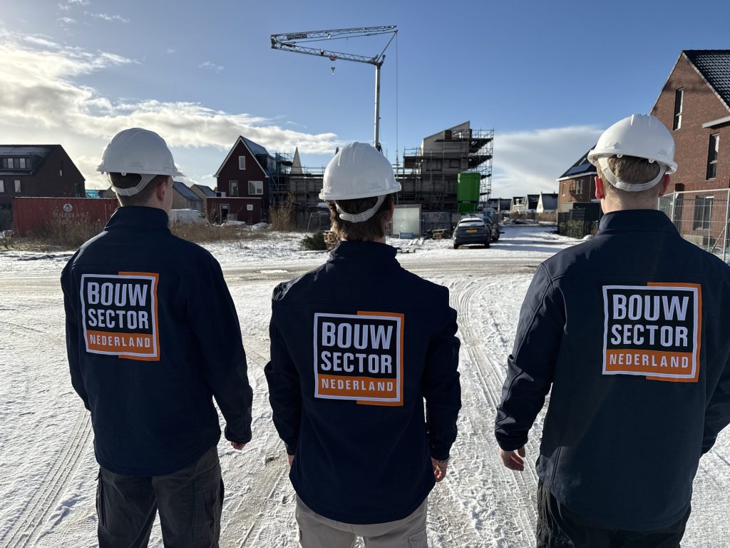 Drie medewerkers van Bouwsector Nederland met helm lopen door een woonstraat in aanbouw