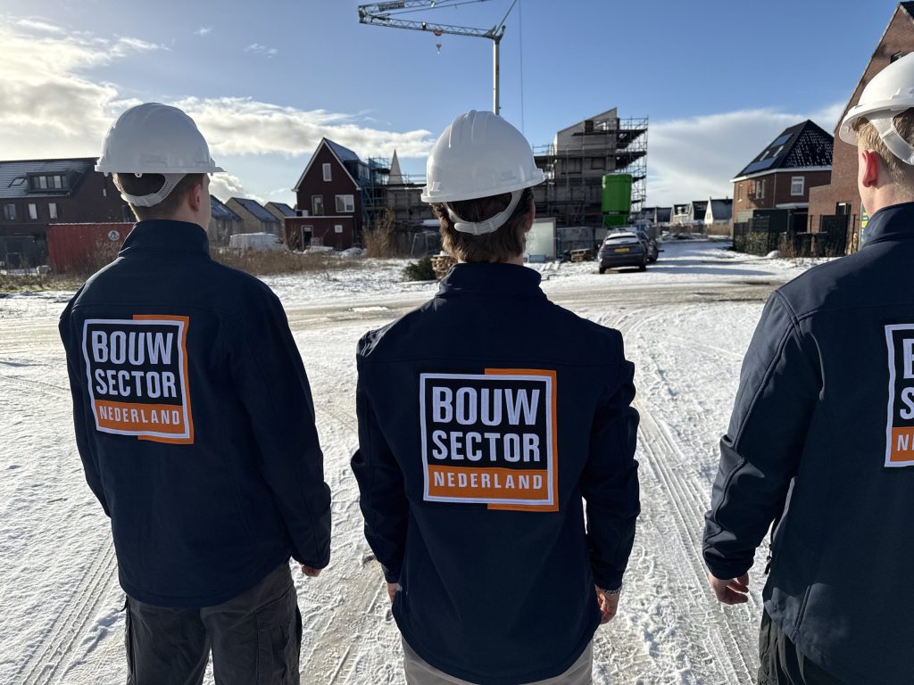 Drie vakmensen van Bouwsector Nederland met witte helm kijken naar een straat met nieuwe huizen